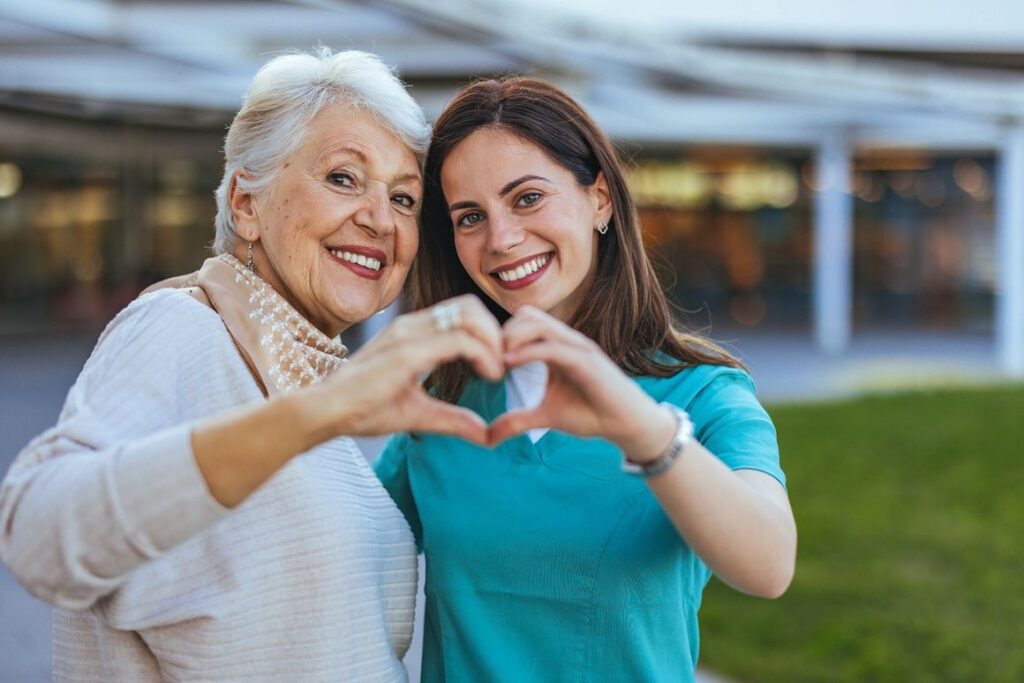 Elderly woman and caregiver making heart shape.