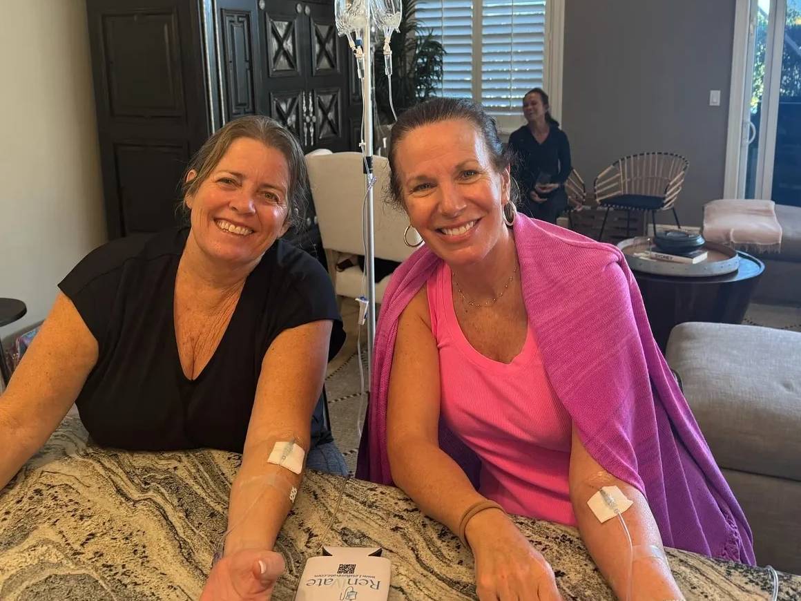 Two women with IV drips smiling indoors.