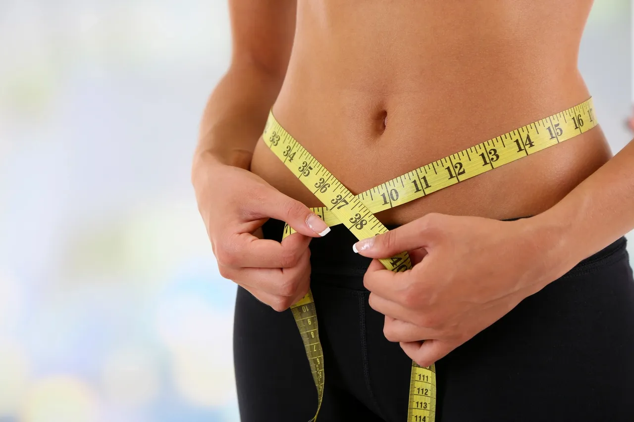 Person measuring waist with yellow tape measure.