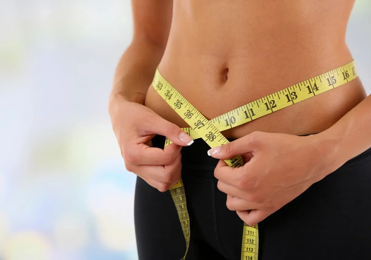 Person measuring waist with yellow tape measure.